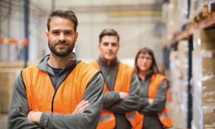 Werknemers met veiligheidsvestje in een magazijn staan in een rij